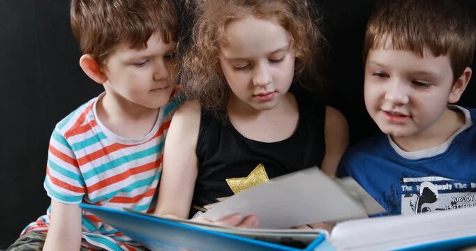 Sister and her brothers sitting on the floor and looking at photo album.