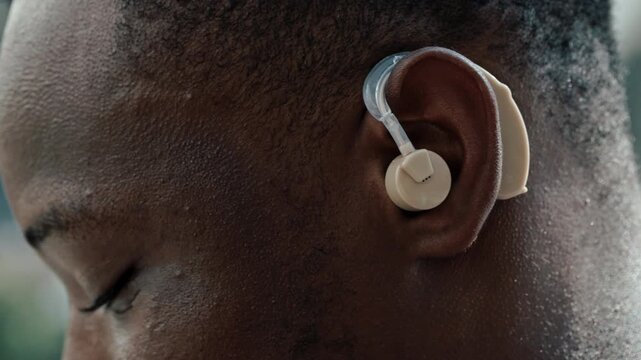 Crop view portrait of African American man with hearing aid on urban backdrop. Businessman with disability integrates in corporate workplace with digital device outdoors closeup