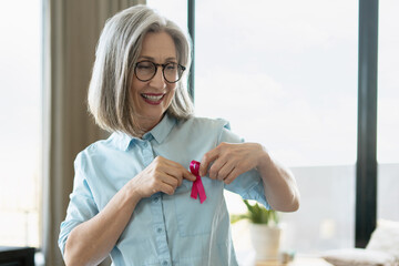 Smiling Senior Woman Pinning Pink Ribbon Showing Support For Breast Cancer Awareness