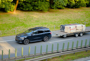 Black SUV Towing Flatbed Trailer Loaded with Palletized Cargo on Highway – Freight and Road Transport Concept