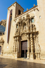 Obraz premium The intricately designed facade of the Basilica de Santa Maria in Alicante, Spain, showcases elaborate stone carvings under bright blue skies, inviting visitors to explore its historical significance