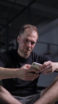 European man looks at his mobile phone with interest. gym. sport. vertical video. man holds phone in hands and reacts emotionally looking at phone screen