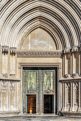 Gothic entrance of Girona Cathedral with weathered green doors, ribbed stone arches, and intricate...