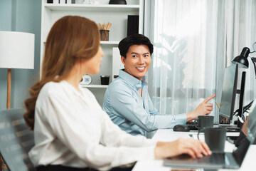 Smiling Asian man talking with woman colleague in planning marketing report project on laptop...