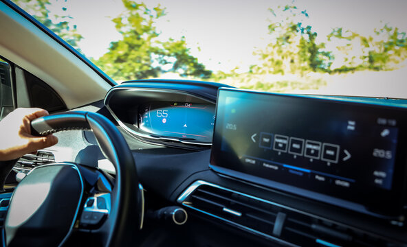Modern digital dashboard view inside a moving car with a driver's hand on the wheel. Navigation system and infotainment screen showing active driving status