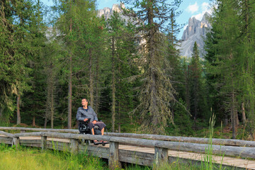 Man with disability enjoys a serene moment on a wooden path through lush greenery in the Dolomites,...