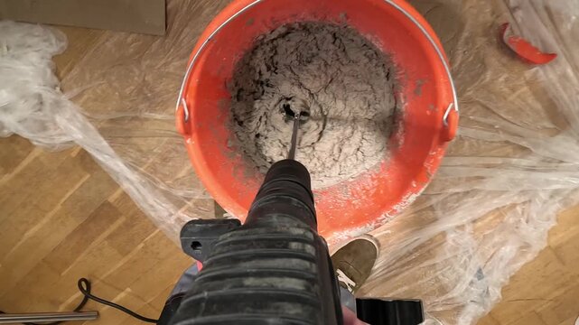 pov Construction worker mixing plaster with a mixing drill in an orange bucket