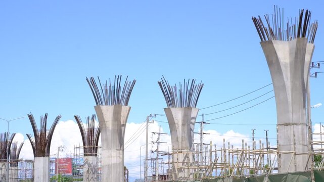 A group of tall concrete pillars are being built. The sky is clear and blue. The pillars are in various stages of construction