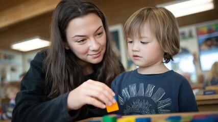 A teacher assists a child with a stacking game in a brightly lit, colorful room designed with adaptive tools for an engaging learning experience.