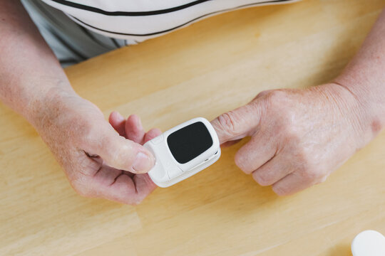 A mature woman measures her pulse using a pulse oximeter.