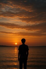 Fototapeta premium Silhouette of young caucasian male watching sunset over ocean