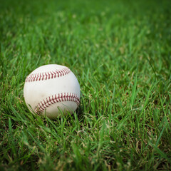 Close-up of a white baseball resting on green grass in an open field.