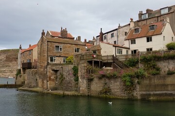 Coastal village scene. Stone buildings with red roofs line a waterway under a cloudy sky  in Staithes - North Yorkshire - United Kingdom