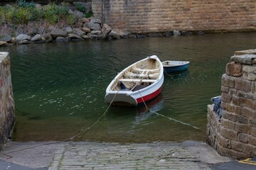 A small white and red boat is tied between stone docks on green water  in Staithes - North...