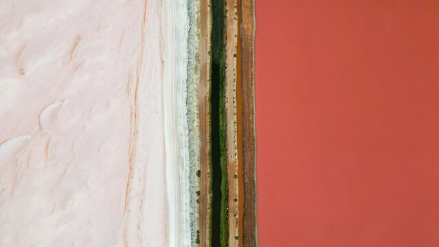 Pink lake next to the coast, divided by streams and streets, seen from above