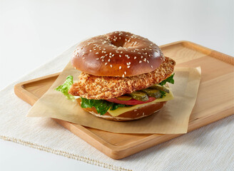 Chicken Schnitzel Bagel Sandwich with Melted Cheese and Pickles on Wooden Tray side view of food...