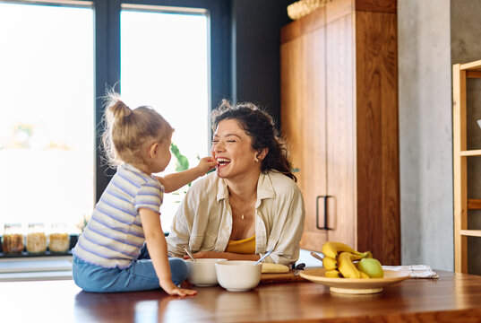 Portrait of a mother and daughter preparing and eating breakfast and having fun in the kitchen at home