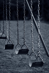 Monochromatic look at a school swing set all in a row. Cool toned black and white representation of a playground swing set with a narrow depth of field.