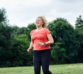 Smiling active mature middle aged woman jogging running in the park