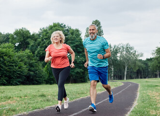 Smiling active mature middle aged couple jogging together in the park