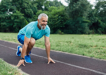 Smiling active mid aged man standing in start position,  jogging running and walking doing fitness...