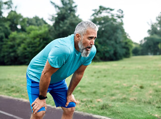 Portrait of a mature mid age man exercising in a park, tired mature female running and taking a...