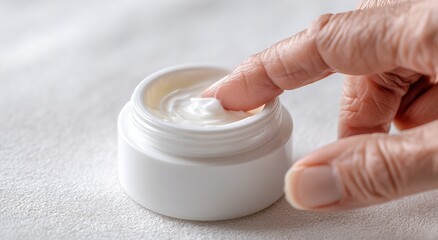 Close-up of a woman's hand applying cream to a jar, against a white background