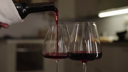 Close-up of unrecognizable person pouring red wine from bottle into two elegant glasses, preparing for wine tasting or special occasion at home. Concept of luxury drink serving, celebration toast.