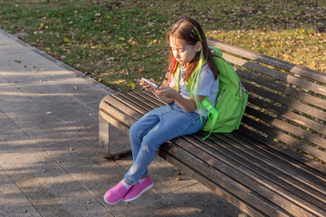 Obraz premium Young girl with backpack using smartphone on park bench on a sunny day
