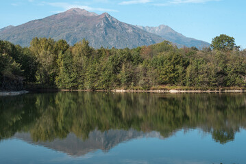 Panoramic view of the Alps in summer with clear blue lake, lush green forests, and dramatic rocky peaks under a bright sky, perfect for travel and outdoor concepts.