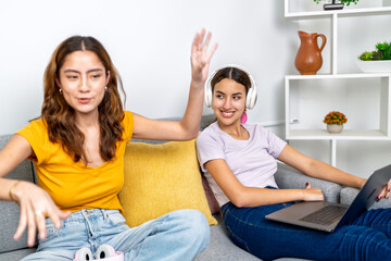 Young women communicating and relaxing on sofa with laptop and headphones