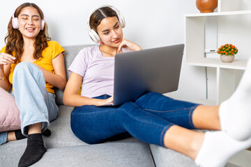 Young students doing homework together, using laptop and headphones at home
