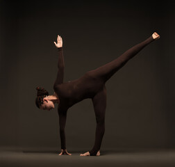 professional yoga girl doing exercises on dark background.young lady in brown sportswear on dark...