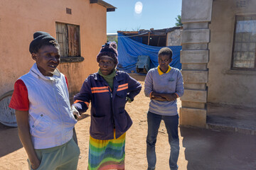 Africa village, three african women chatting in the yard, sunny day, poverty in rural areas