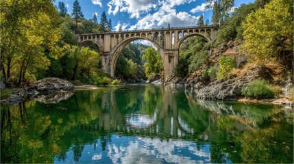 Fototapeta premium Beautiful scenic bridge spanning river with reflection in calm water under bright sky