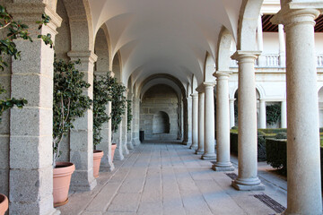 Outdoor passage with many white stone arches and columns with potted plants in courtyard of...
