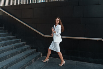 A smiling woman in an office setting, engaging in a phone call while using a tablet.