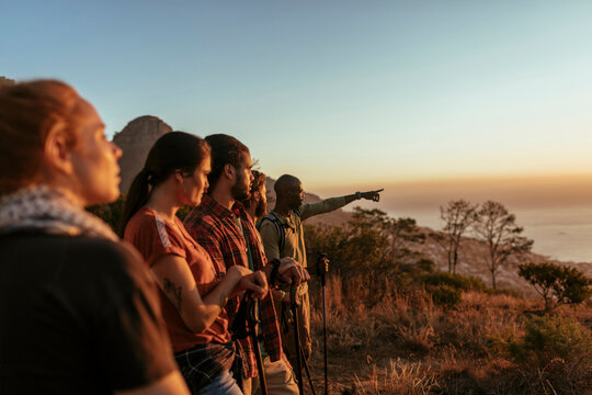 Diverse group of young people hiking and taking a moment to look at the beautiful sunset and ocean