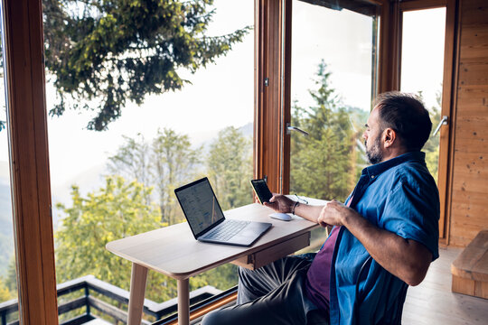 Man remote working in mountain cabin with forest view