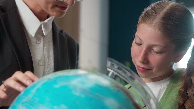 Happy laughing curious Caucasian teenager junior school little girl child smiling student kid schoolgirl study geography globe world map magnifying glass with teacher female woman professor classroom