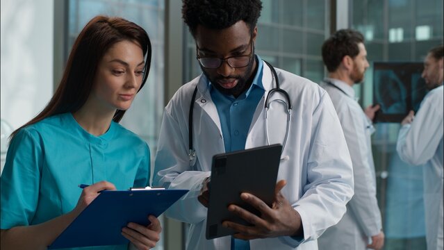Two doctors discussing patient medical examination results Caucasian woman therapist doctor talk with African American man surgeon physician teamwork using digital tablet clipboard at hospital clinic