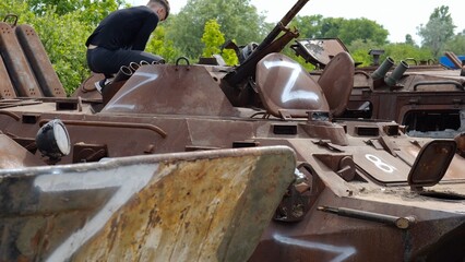 Young man looking at destroyed military equipment of the russian army. Exhibition of rusty and...