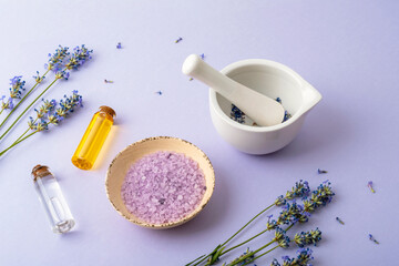 Lavender flowers with essential oils and salt for spa treatment on pastel purple background. Top view