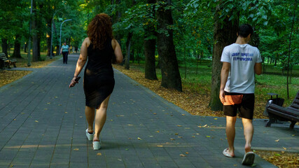 People walking on a tree-lined path in a park during a sunny day in summer