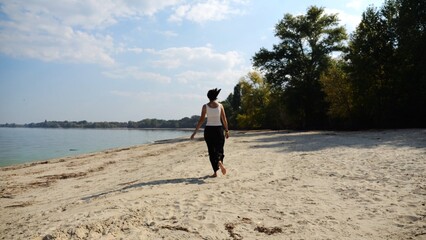 Happy adult woman jogging on sandy beach near shoreline at sunny day. Beautiful lady running on seashore with calm waves at background. Concept of summer vacation or holiday. Slow motion