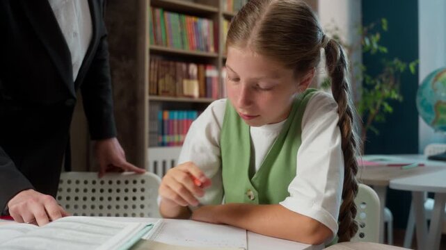 Caucasian teacher female woman smiling professor helping student pupil correcting mistake answer teaching little girl child school kid writing pen task tutor showing thumb up gesture indoor classroom