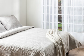 Minimalist cozy bedroom with soft quilted beige bedspread, textured blanket and sheer white...