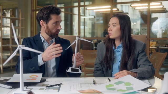 Sustainable solutions graph analysis wind energy discussion teamwork Korean businesswoman Caucasian business man expert review charts clean tech innovation eco planning strategy development blueprint