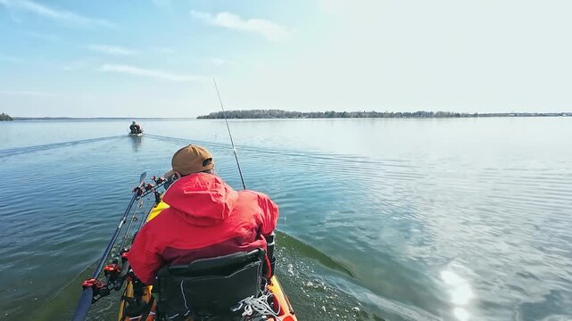 Angler or fishermen in dry suit on motorized pedaling fishing kayak trolling during fishing game tournament in the lake water. Kayak fishing and watersport. Water sport in spring.