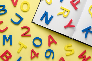 A notebook and colorful alphabet letters and numbers scattered on light yellow background. Back to school concept.